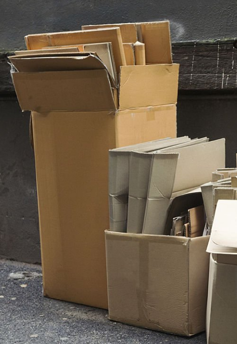Several cardboard boxes are lined up next to a fence and filled with flat folded boxes and cardboard standing upright inside them. Several cardboard boxes are lined up next to a fence and filled with flat folded boxes and cardboard standing upright inside them.